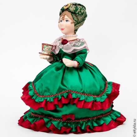 Doll warmer on a teapot with a cup of tea in a green dress